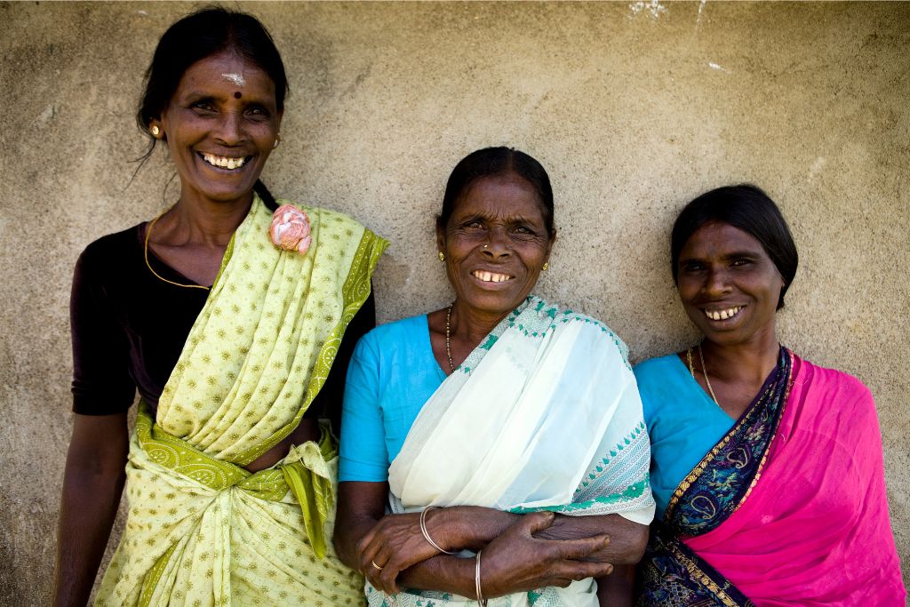 Three women in vibrant sarees pose against a rustic wall, showcasing Sri Lanka’s traditional dress and friendly hospitality. Great inspiration for Sri Lanka traditional clothing and packing tips.