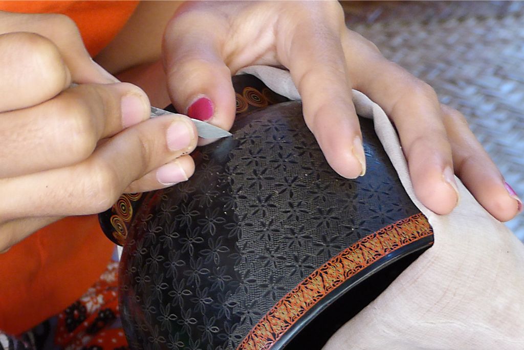 A craftsman carefully etching intricate designs on a black lacquered bowl, a fine example of Sri Lankan lacquerware. This unique handicraft makes an exquisite gift from Sri Lanka for collectors of traditional art.