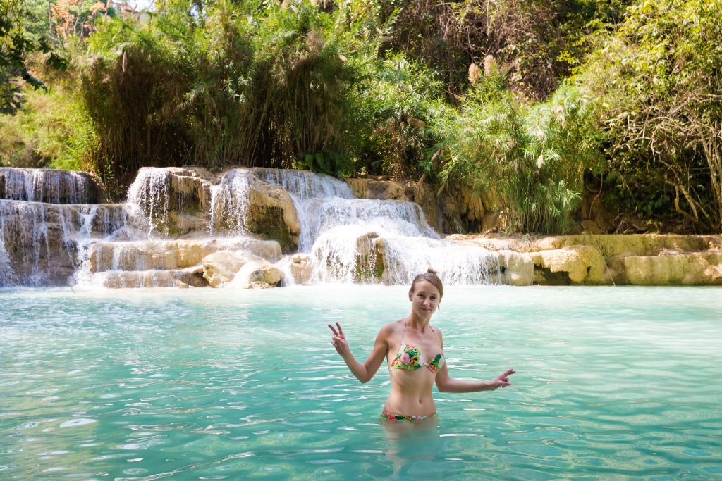 A woman stands waist-deep in the turquoise pool of Kuang Si Falls in Laos, framed by cascading waterfalls and lush jungle. Laos offers one of the most serene and off-the-beaten-path winter getaways in Asia, ideal for nature lovers and tropical adventurers escaping colder climates.
