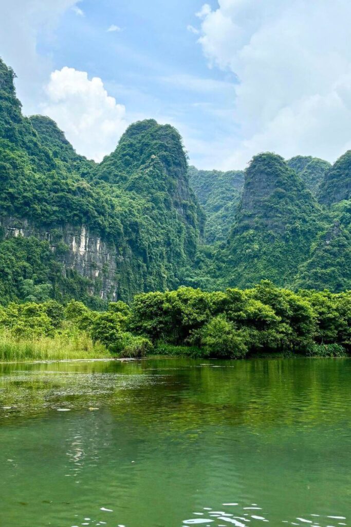 Lush, forest-covered limestone karsts rise above a calm river in Ninh Binh, Vietnam, with reflections of greenery on the water. This scenic region offers peaceful river cruises and dramatic landscapes, making it one of the most underrated winter destinations in Asia for eco-tourism and adventure.
