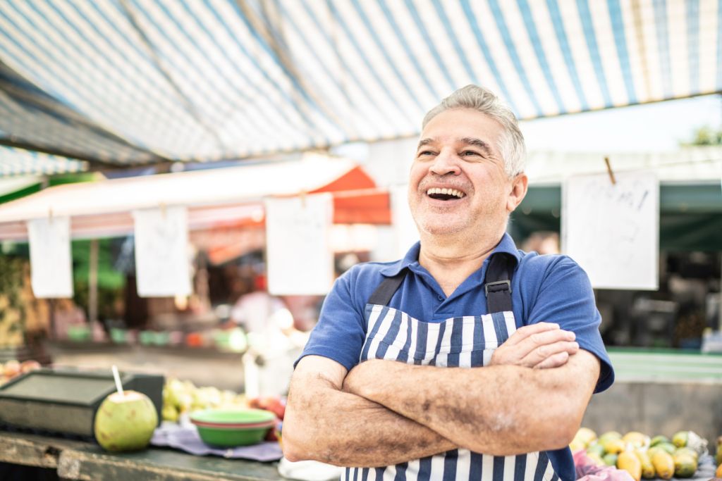 A smiling vendor wearing an apron in an open market, showcasing the friendly atmosphere where travelers can practice bargaining tricks