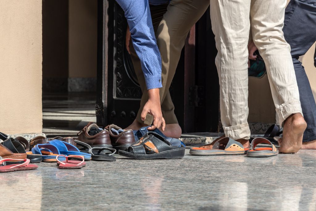 A group of men leaving or entering a mosque, with various sandals and shoes scattered outside the entrance, symbolizing adherence to Islamic etiquette and mosque rules. This scene captures the cultural and religious practices of mosques in Egypt.