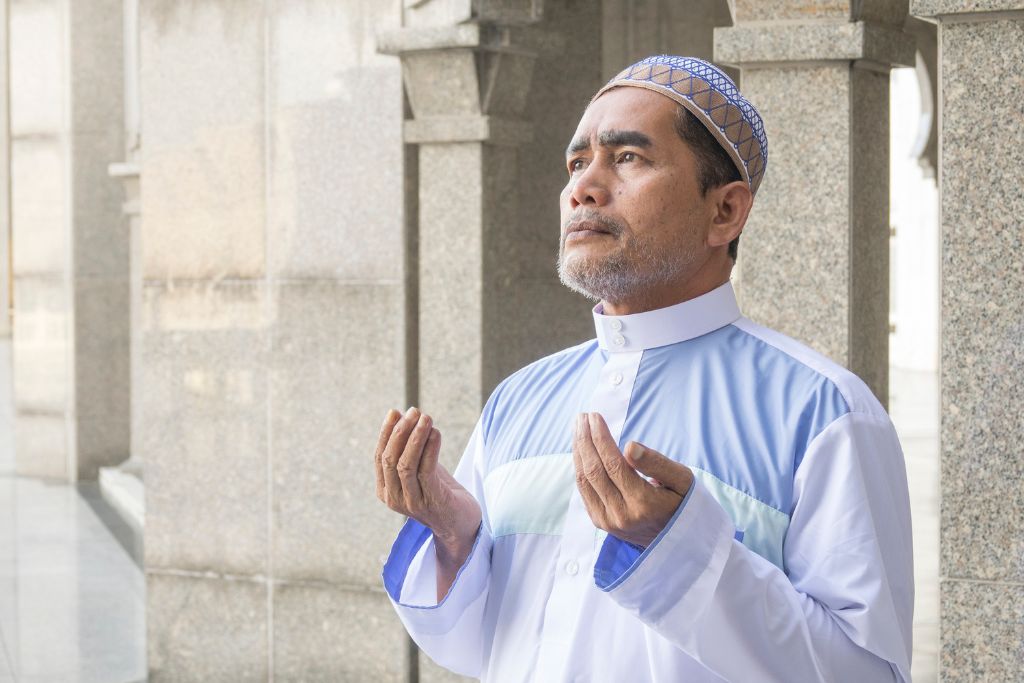 A man dressed in traditional Islamic attire, standing in prayer at an Egyptian mosque, surrounded by ornate stone columns. This portrays the spiritual essence of Islamic culture and prayer in Egypt.