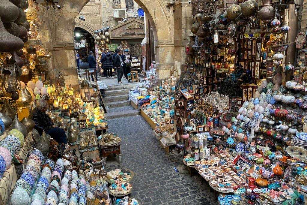 Packed market stalls in Khan el Khalili, Cairo, showcasing Egyptian souvenirs such as colorful lanterns, pottery, and jewelry in a lively bazaar environment.