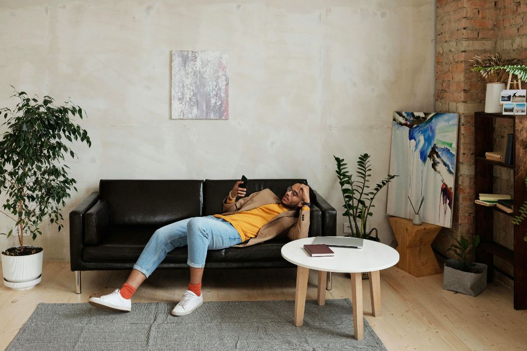 A man lounges on a black couch, looking at his phone in a stylish, minimalist living room. Knowing how to bargain while on vacation can leave you with extra money for relaxation. Avoiding overpaying means more budget for experiences.