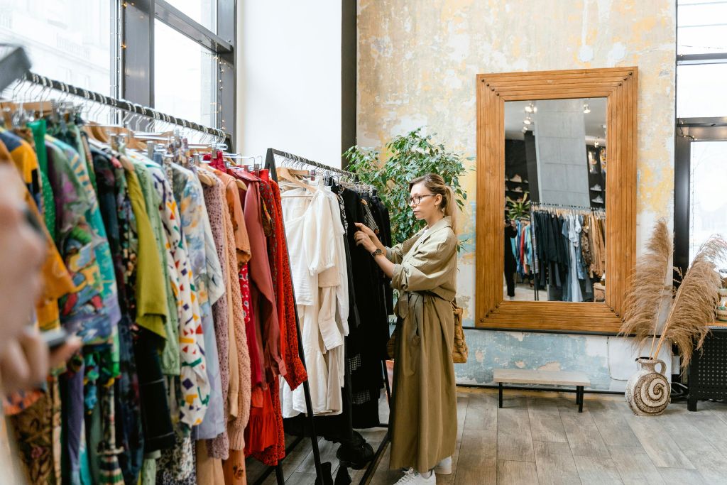 A woman in a long trench coat browses a rack of colorful clothing in a stylish boutique. If you want to save money while traveling, learning how to haggle while traveling in markets and stores can help you get the best deals.