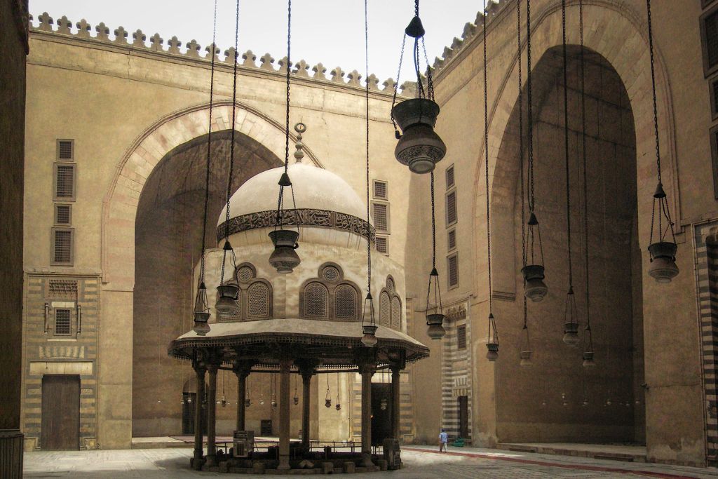 A close-up of the Al-Hakim Mosque interior in Cairo, showcasing its intricate arches, hanging lanterns, and domed prayer area. This highlights Islamic Cairo's rich religious and architectural history.