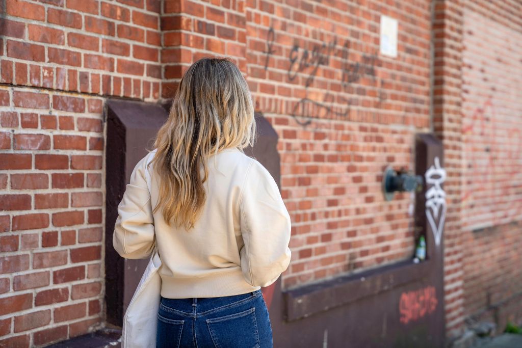 : A woman in a cream jacket and jeans walks past a brick wall with graffiti. If you’re visiting a new city, knowing how to haggle respectfully can make shopping more affordable. Avoid being taken advantage of and stop overpaying.