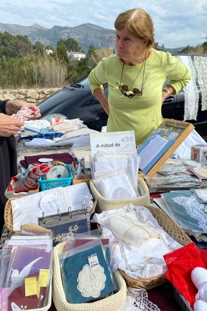 woman in a lime green shirt stands behind a table of lace and fabric goods, looking skeptical. This vendor might not accept just any offer—haggling tips and patience are key. Always remember the first rule of haggling: be prepared to walk away.