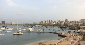 A lively view of Alexandria's harbor, with boats of various sizes docked against a backdrop of modern city buildings. One of the best stops on a Cairo to Alexandria day trip.