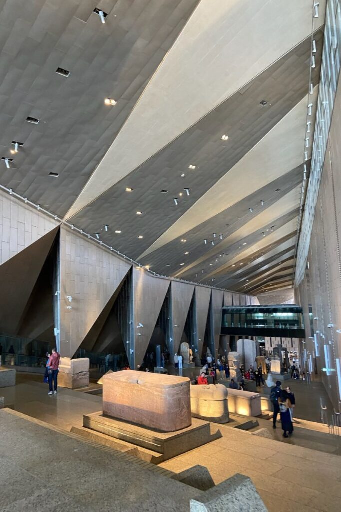 A spacious hall inside the Grand Egyptian Museum Giza, displaying massive ancient sarcophagi and artifacts under a high, angular ceiling—one of the top things to see at the Grand Egyptian Museum.