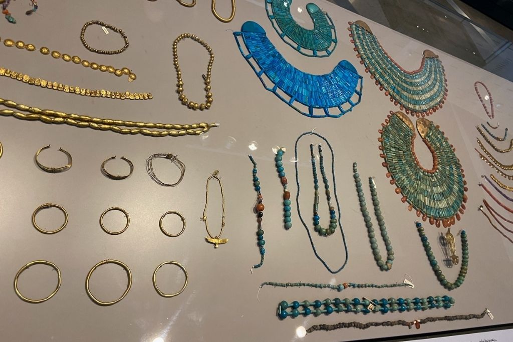 A display case featuring intricate gold and turquoise jewelry from ancient Egypt inside the Grand Egyptian Museum shop, one of the must-visit stops for history lovers and those looking for Grand Egyptian Museum souvenirs.