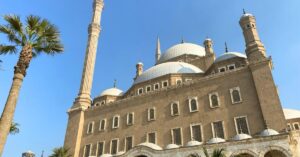 The exterior of the Mosque of Muhammad Ali, also known as the Alabaster Mosque, in Cairo, Egypt, with towering minarets and domes under a clear blue sky. This is one of the most famous mosques in Egypt, located inside the Citadel of Cairo.