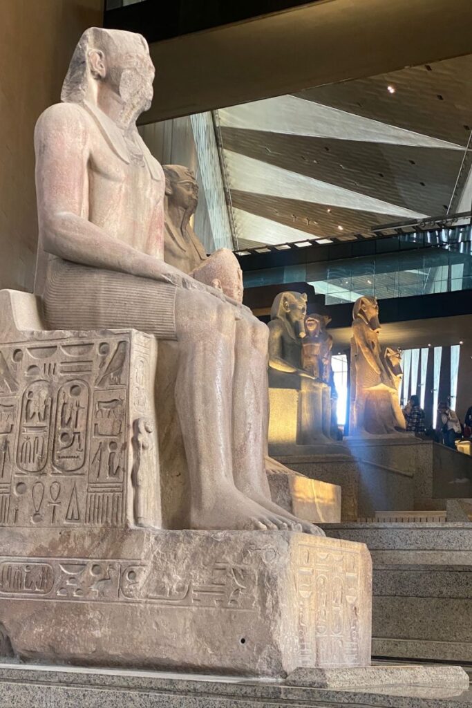 A row of massive, seated statues of ancient Egyptian rulers displayed along the Grand Egyptian Museum staircase, demonstrating the vast Grand Egyptian Museum size.