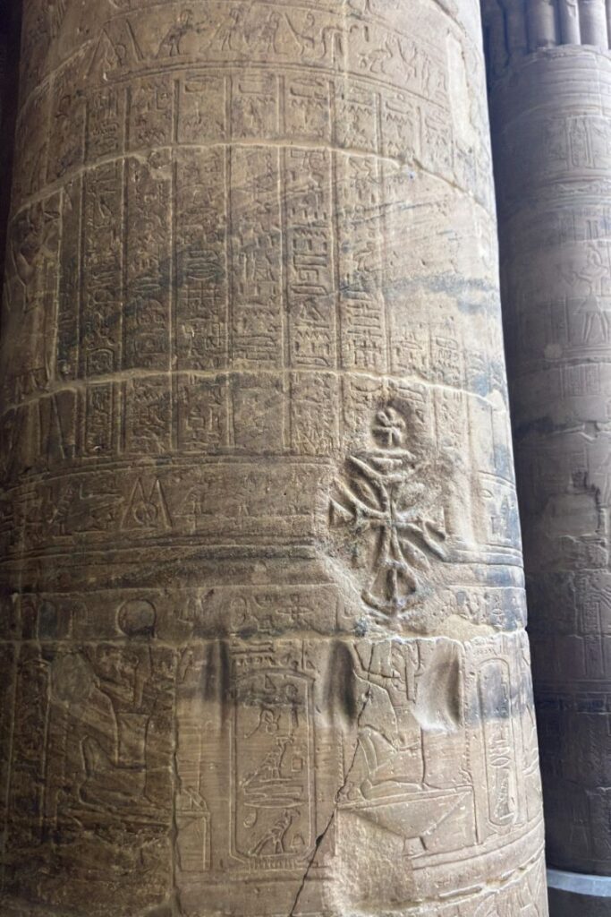 Close-up of a column inside the Temple of Isis at Philae, Egypt, with detailed hieroglyphs and a prominent Coptic cross carved over ancient script, symbolizing the temple's layered religious history.
