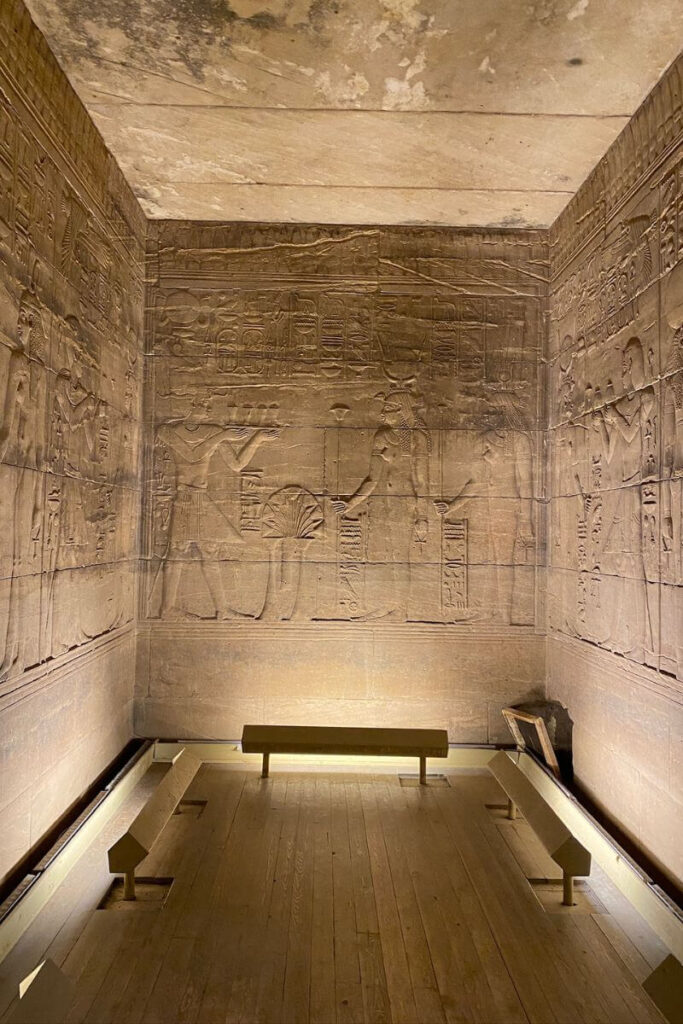 Illuminated sanctuary room inside the Philae temple complex, Egypt, showing walls covered in intricate carvings of Egyptian gods and rituals, part of the Temple of Isis on Philae Island.