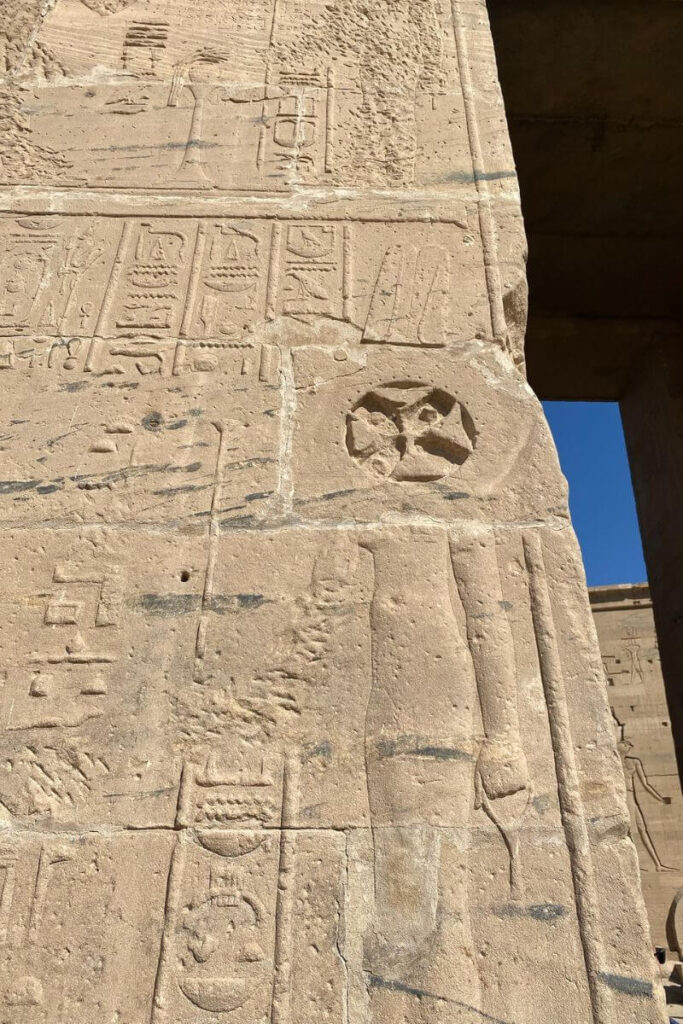 Wall of the Temple at Philae on Aswan Island, Egypt, with weathered hieroglyphs and a visible Coptic cross carved into the sandstone, reflecting the temple’s transition from ancient to Christian use.