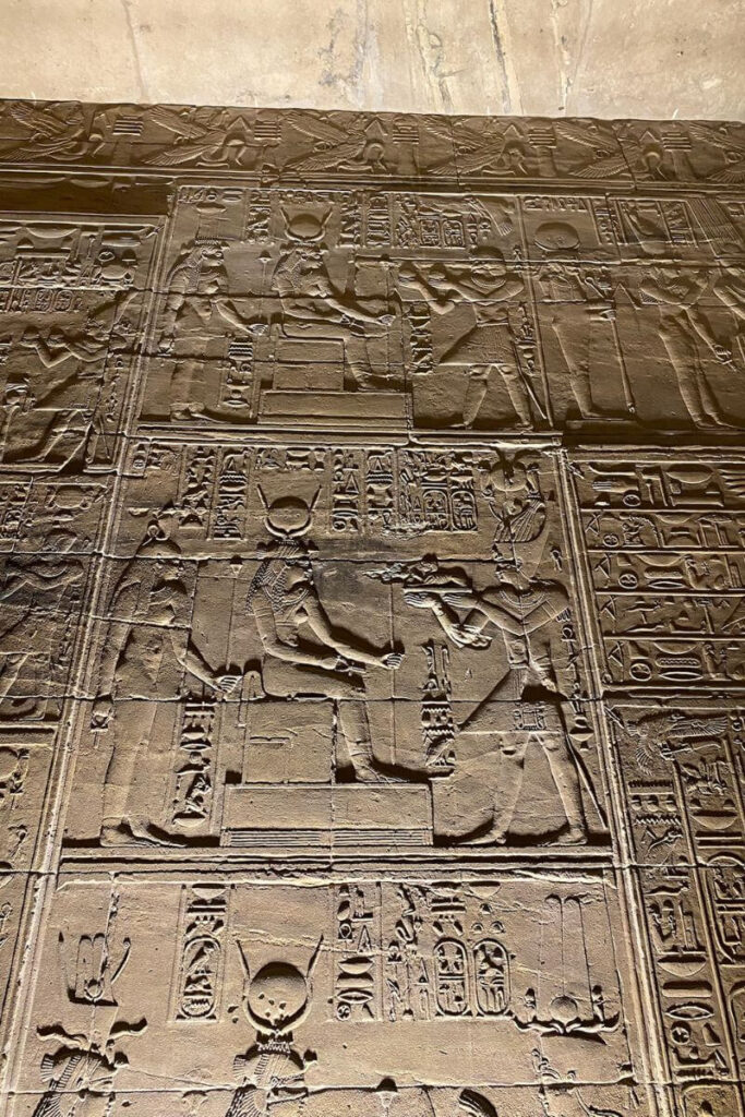 Carved relief inside the Temple of Isis at Philae, depicting a seated goddess receiving offerings, surrounded by hieroglyphic inscriptions, highlighting the sacred role of Isis in Philae temple history.