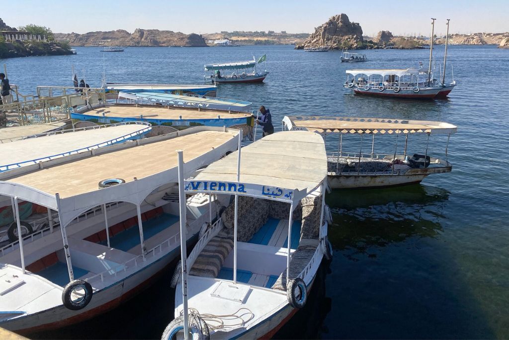 Traditional boats docked near Aswan Island and sailing across the Nile River toward Philae Island Egypt, a key access point for visiting the Temple of Isis Egypt and the historic Temples of Philae.