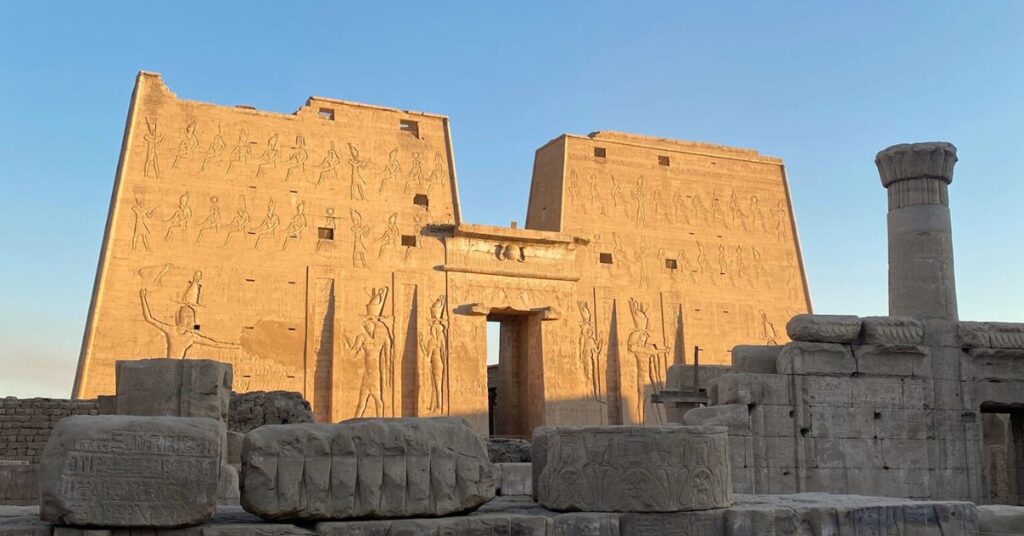 Golden sunlight hits the monumental pylon entrance gate of the Temple of Horus in ancient Egypt, with towering carvings of deities and pharaohs—one of the most iconic features of the Edfu Temple and a prime example of pylon Egypt architecture.