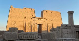 Golden sunlight hits the monumental pylon entrance gate of the Temple of Horus in ancient Egypt, with towering carvings of deities and pharaohs—one of the most iconic features of the Edfu Temple and a prime example of pylon Egypt architecture.