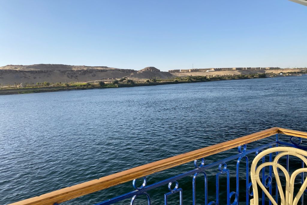 Serene view of the Nile River with a temple cruise railing in the foreground and desert cliffs in the distance—a peaceful moment on a Temple Nile cruise exploring Edfu and beyond.