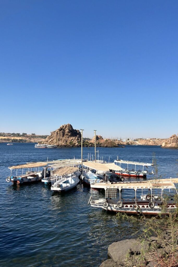 boats ferrying tourists across the Nile toward the Temple at Philae, Egypt, with the temple structure visible in the distance, emphasizing access from Aswan Island to Philae Island.