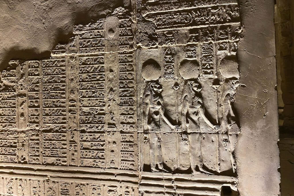 Detailed carvings of Egyptian gods on stone walls at night in Kom Ombo Temple, showcasing the artistry tied to crocodile headed god Sobek and ancient Egyptian spiritual life.