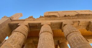 Massive stone columns with intricate carvings inside an ancient Egyptian temple, viewed from below against a bright blue sky. This awe-inspiring view adds perspective to the debate around is Egypt worth visiting and offers contrast to common reasons not to go to Egypt.