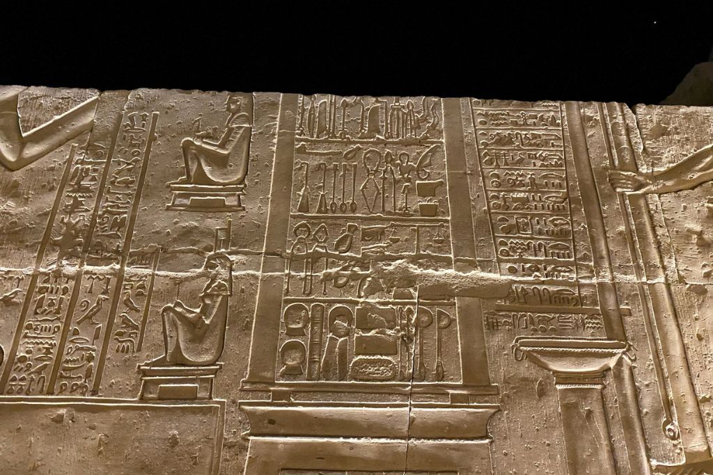 Nighttime image of Kom Ombo Temple carvings showing seated deities and symbols of crocodile worship, part of a dual temple dedicated to Sobek, the Egyptian crocodile god, and Horus.