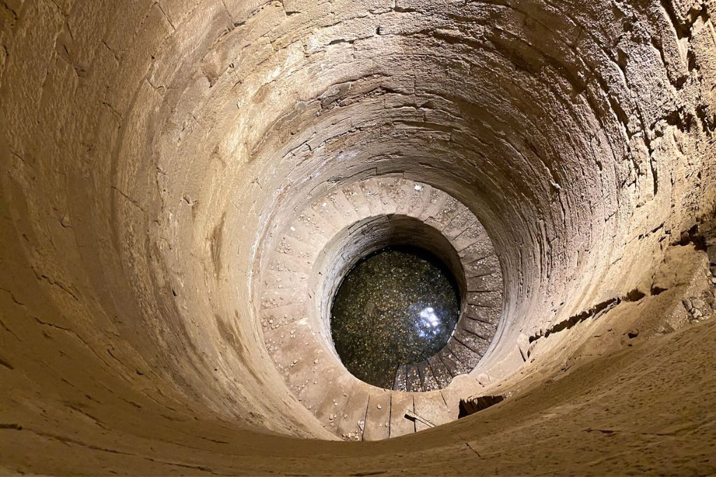 A deep, circular stone well at the Temple of Kom Ombo, partially filled with water, reflecting light—part of ancient water rituals associated with crocodile worship and Egypt’s crocodile god Sobek.