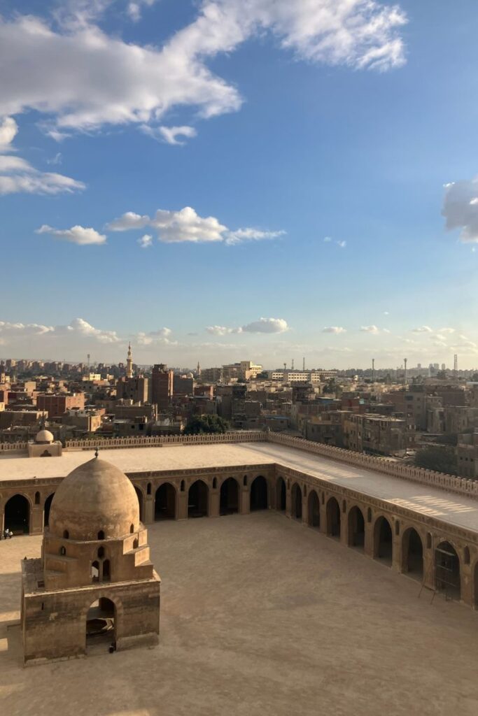 A scenic view of the skyline of Cairo, with the Mosque of Ibn Tulun in the foreground under a sky full of soft clouds. Highlights the historic yet urban vibe for those debating “is Cairo worth visiting.”