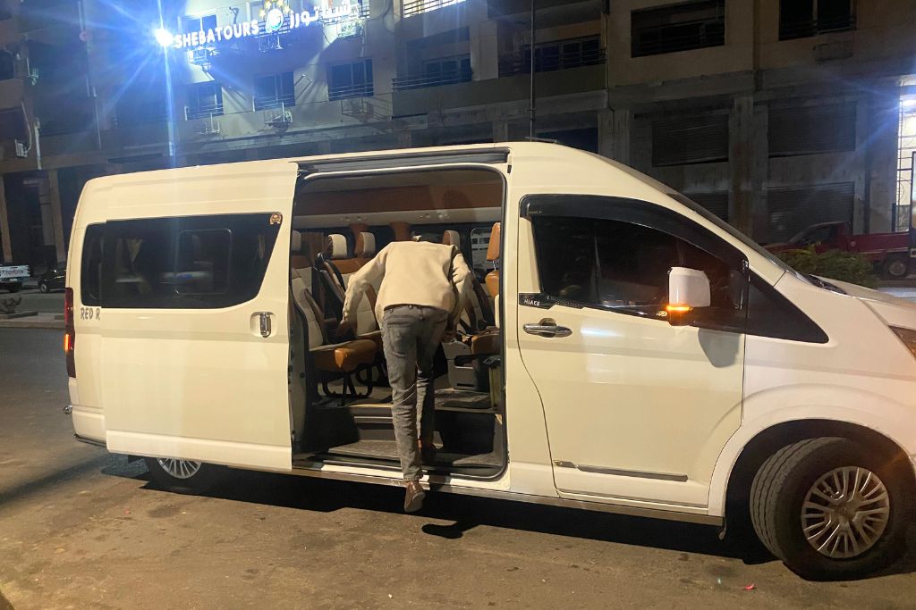 A man boarding a modern white minibus-style shuttle van at night, representing private or shared transport alternatives to Uber in Egypt. Ideal for readers comparing Uber in Egypt price to other local transport options from Cairo to Hurghada or Sharm El Sheikh.