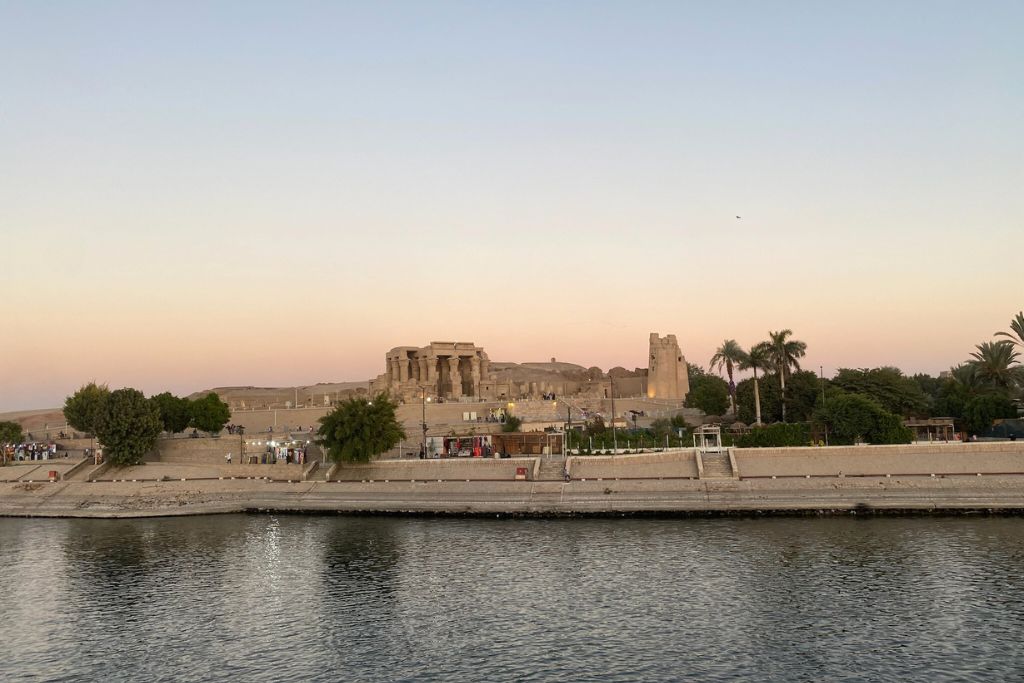 Distant sunset view of Kom Ombo Temple from across the Nile, capturing the temple’s grandeur and its connection to Sobek, the crocodile-headed god of ancient Egyptian mythology.