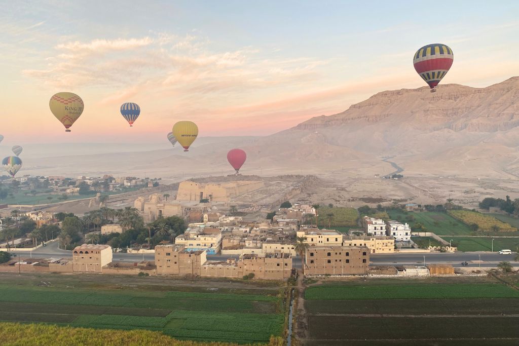 Multiple hot air balloons float above fields and ruins near Luxor at sunrise, offering stunning views of the landscape and history. A dreamlike experience and a top reason why people should visit Egypt.