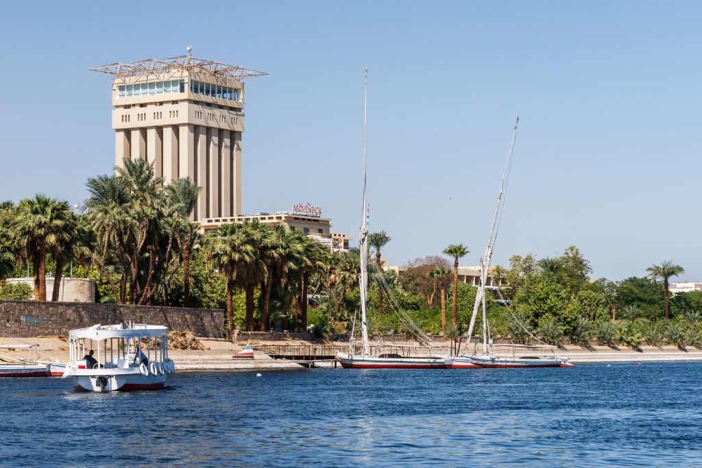 View of the Mövenpick Resort Aswan and its iconic tower rising above palm trees along the Nile River, a standout among Aswan hotels and a top pick for travelers looking for luxury hotels in Egypt.