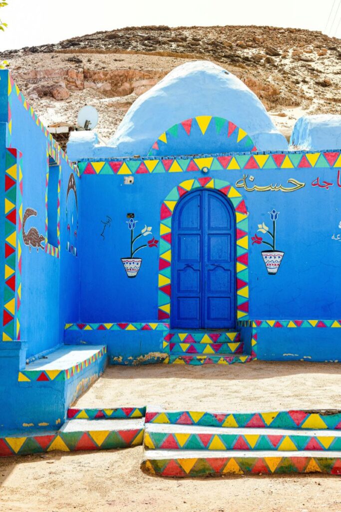 Brightly painted blue Nubian house in a Nubian village on Elephantine Island, Aswan, featuring geometric patterns and floral pot motifs that reflect Nubian architectural art in southern Egypt.