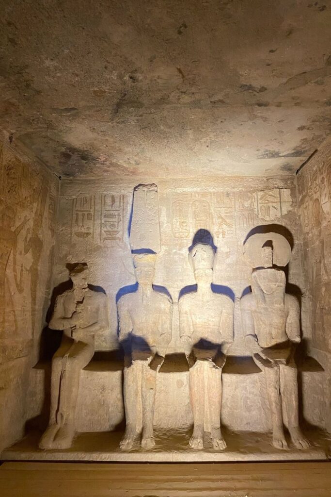 Dimly lit chamber inside Abu Simbel featuring four large seated statues of gods and pharaohs; part of the temple's innermost sanctuary, a must-see highlight for anyone planning a day trip from Aswan to Abu Simbel.