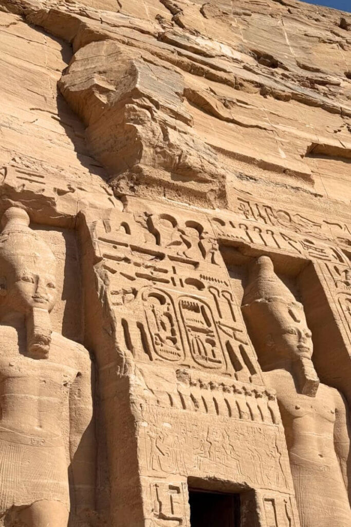 Close-up view of the detailed carvings and partially damaged statue on the façade of Abu Simbel Temple, highlighting the intricate hieroglyphics and craftsmanship. An essential stop for travelers following a guide to visiting Abu Simbel in Egypt.