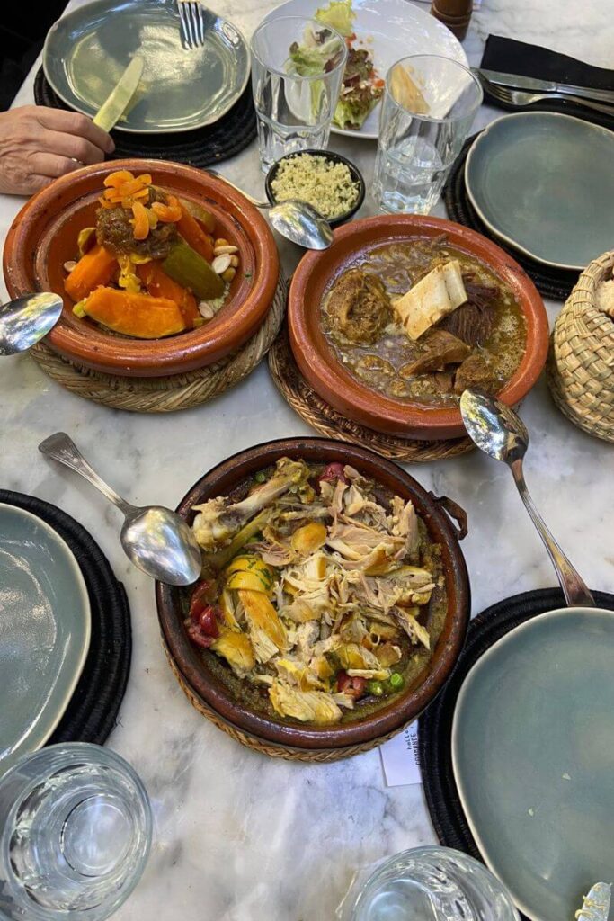 Three Moroccan-style tagines full of hearty meats and vegetables on a shared table, evoking community meals and emphasizing the contrast for those eating out alone. Useful for showing the emotional aspects of going to a restaurant alone.