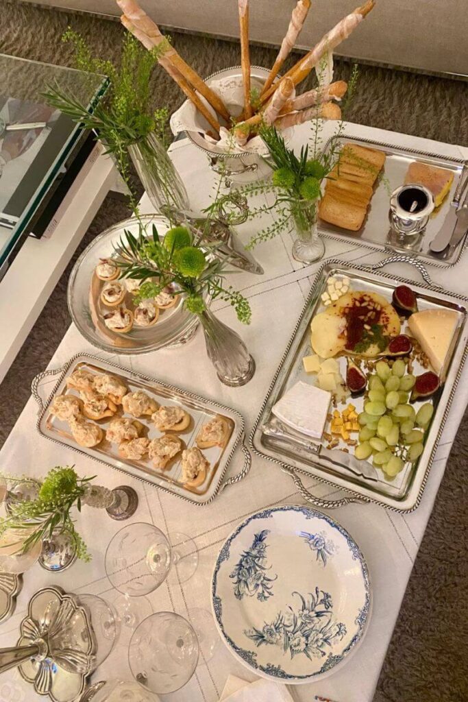 Overhead shot of a cheese and snack buffet with carrots, pâté, grapes, and mini desserts at a dimly-lit gathering. Conveys the social setting that often makes people question, "Is it weird to go to a restaurant alone?"