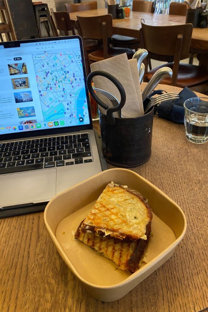 Grilled sandwich and laptop on a wooden café table, representing eating lunch alone during a workday. A realistic look at eating out alone and how to eat alone in a restaurant without feeling awkward.