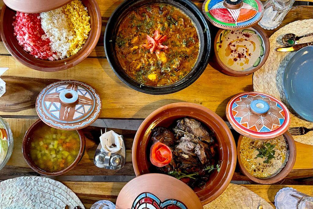 Top-down view of a traditional Nubian meal in a Nubian village in Aswan, Egypt, showing colorful rice, hearty stews, and vegetables served in painted clay dishes typical of the Nubian Village Hotel or similar local hospitality.