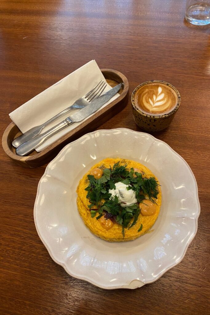 Fluffy omelet topped with herbs beside a latte, perfect for eating breakfast alone in a cozy café. This image reflects how to dine alone confidently and make solo dining part of your travel routine.