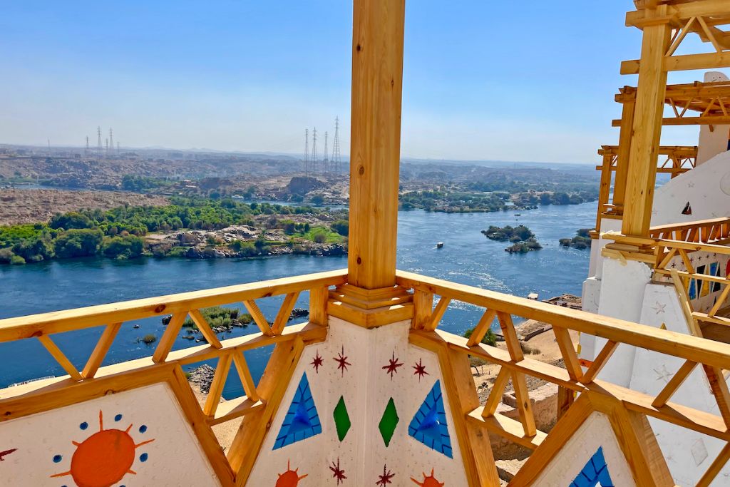 A balcony view from a Nubian-style guesthouse in Aswan, Egypt, overlooking the Nile River and the lush greenery of Elephantine Island, showcasing the serene beauty of Nubian Egypt.