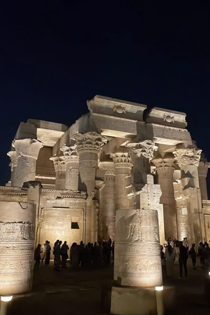 Kom Ombo Temple in Egypt lit up at night, revealing its symmetrical architecture and detailed column carvings as visitors gather in the temple courtyard. Known for its twin dedication to Sobek and Horus, it’s a standout among Egyptian temples.