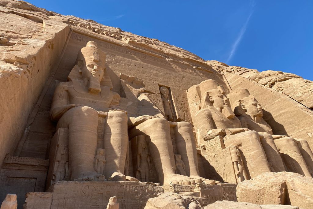 Towering statues of Ramses II carved into the facade of Abu Simbel under a bright blue sky; an iconic view for those traveling from Aswan to Abu Simbel or taking an Abu Simbel tour from Aswan.
