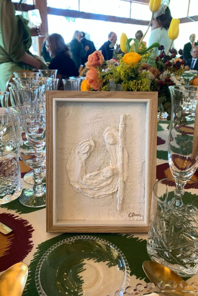 Elegant wedding or event table setting featuring a framed textured artwork centerpiece, surrounded by glassware and bright floral arrangements. Symbolizes being solo at a formal gathering and highlights the visual contrast of dining alone versus group settings.