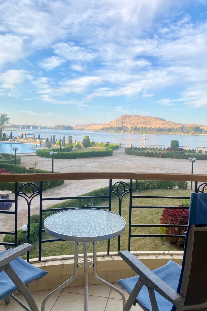 Scenic view from a hotel balcony in Aswan, overlooking manicured gardens, a pool, and the Nile River with a desert hill in the distance — an ideal spot when searching for hotels in Aswan Egypt 5 star or best hotels in Aswan.