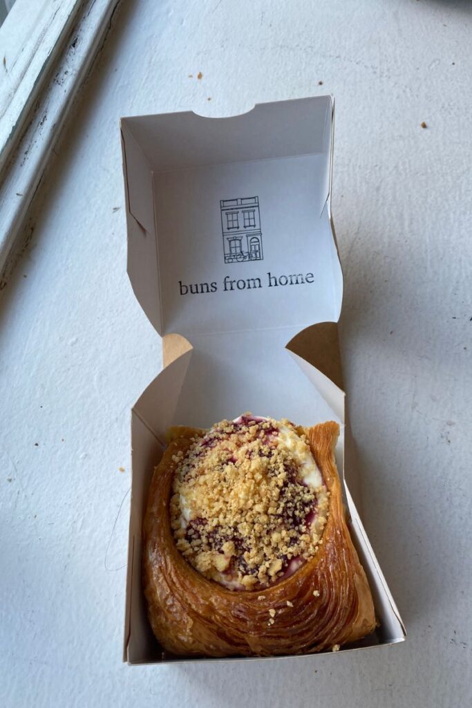 Flaky pastry in a takeaway box labeled “buns from home,” ideal for eating by yourself on the go. Highlights alternatives to dining alone and eating alone while traveling without social anxiety.